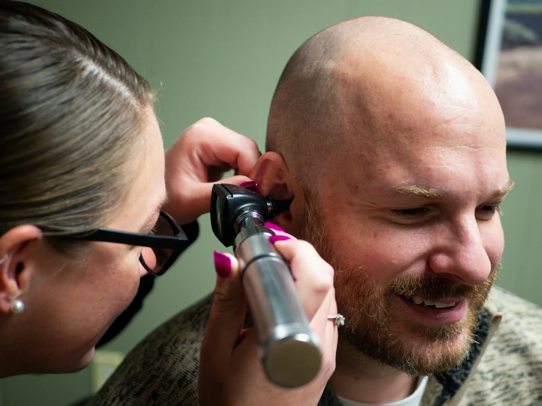 A hearing care professional examining a smiling patient's ear with an otoscope
